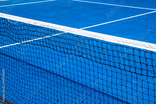 Blue tennis court with net. Empty sport field photo. Hard court cover for lawn tennis. Summer sport activity outdoor. White markup on blue court. Sunny day on tennis court. Sport field in park