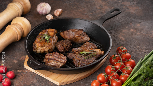 The different types of fried steak in frying pan, close up view. The different types of fried meat. Vegetables, herbs, spices. Tomato, garlic, pepper, salt. Dark background. High quality photo
