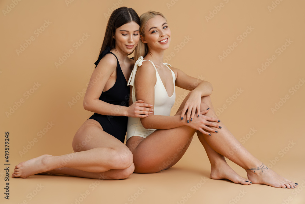 Happy two women wearing swimsuits hugging while sitting on floor Happy two women wearing swimsuits hugging while sitting on floor