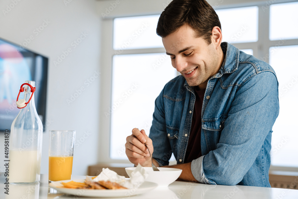 Happy handsome young man smiling while having breakfast at home Happy handsome young man smiling while having breakfast at home