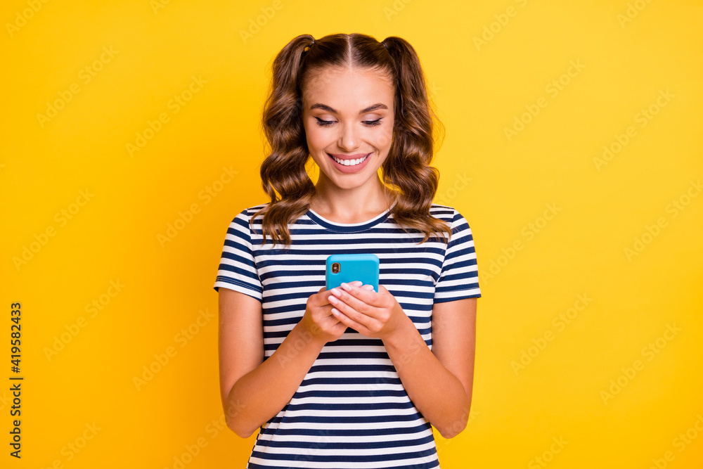 Photo of charming pretty young lady dressed striped outfit typing modern device isolated yellow color background Photo of charming pretty young lady dressed striped outfit typing modern device isolated yellow color background