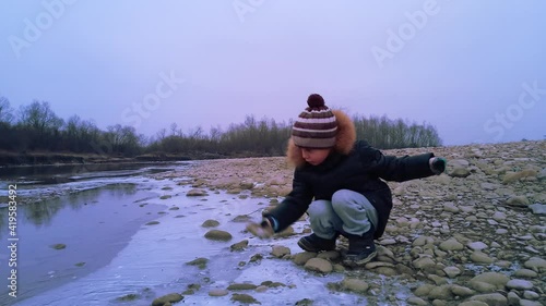 Little boy playing near a mountain river in winter