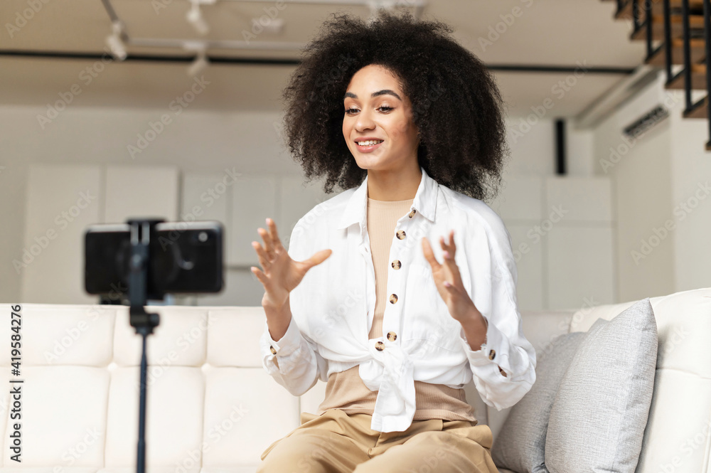 © Vadim Pastuh - Smiling female African American blogger influencer sitting at phone on stabilizer, recording new video for subscribers or streaming educational lecture, sharing knowledge live online at home office © Vadim Pastuh - Smiling female African American blogger influencer sitting at phone on stabilizer, recording new video for subscribers or streaming educational lecture, sharing knowledge live online at home office
