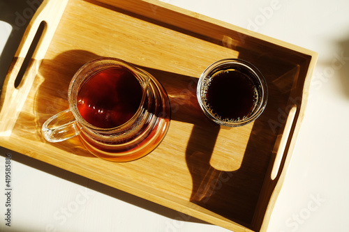 Freshly brewed black filter coffee is served on a bamboo tray on sunlit white table. Top view