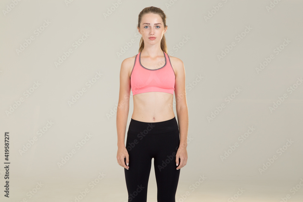 Sporty woman in a pink t shirt looks at the camera, isolated on a gray yellow background. Sporty woman in a pink t shirt looks at the camera, isolated on a gray yellow background.