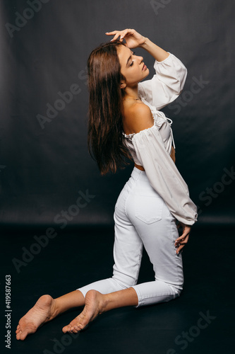 Amazing girl with a beautiful figure sitting on a floor at black background in the studio.
