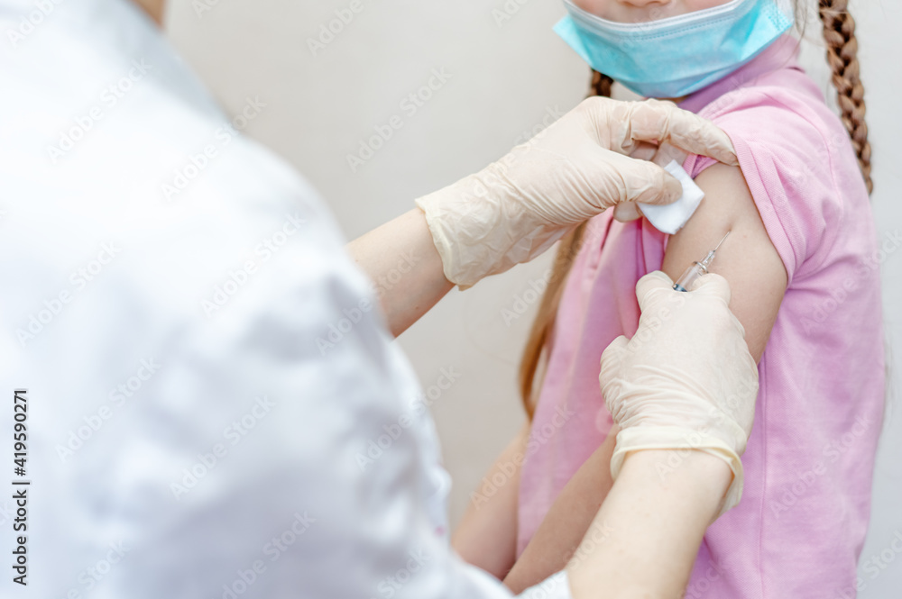 The hand of a nurse treats the girl's shoulder with a napkin with an antiseptic for an injection, injection into the arm. Syringe with vaccine medication in the doctor's hand. Vaccination of children The hand of a nurse treats the girl's shoulder with a napkin with an antiseptic for an injection, injection into the arm. Syringe with vaccine medication in the doctor's hand. Vaccination of children