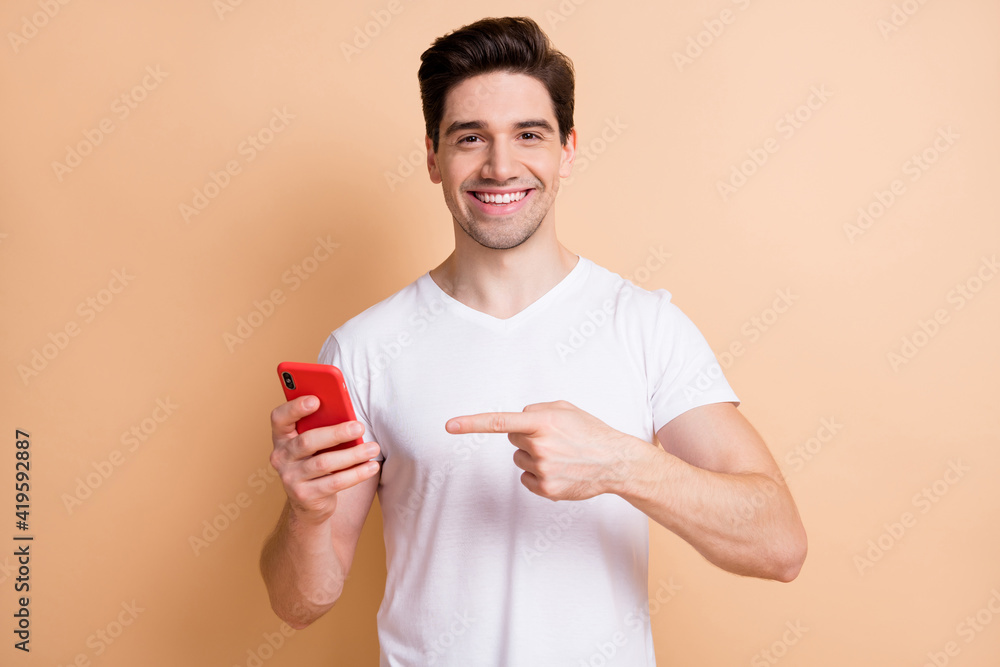 Portrait of handsome young person indicate finger phone toothy smile isolated on beige color background