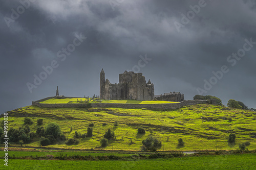 Rock of Cashel castle on green hill illuminated by sunlight with storm clouds in background. Known as Cashel of Kings or St. Patricks Rock  Ireland