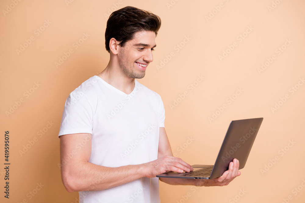 Portrait of half turned handsome cheerful guy using netbook write message isolated on beige color background Portrait of half turned handsome cheerful guy using netbook write message isolated on beige color background