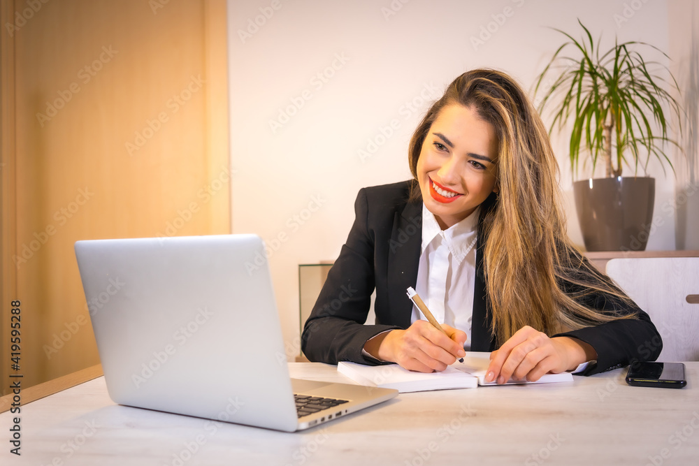 Teleworking at home during the coronavirus pandemic, young blonde Caucasian woman taking notes at online video call meeting Teleworking at home during the coronavirus pandemic, young blonde Caucasian woman taking notes at online video call meeting