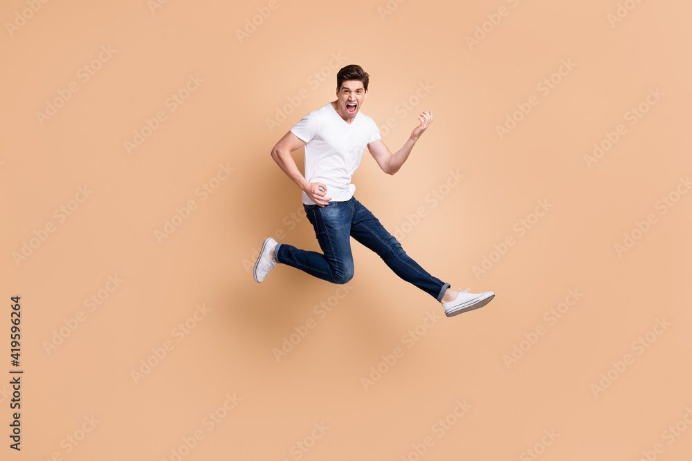 Full size profile photo of hooray brunet man jump play guitar yell wear t-shirt jeans sneakers isolated on beige color background