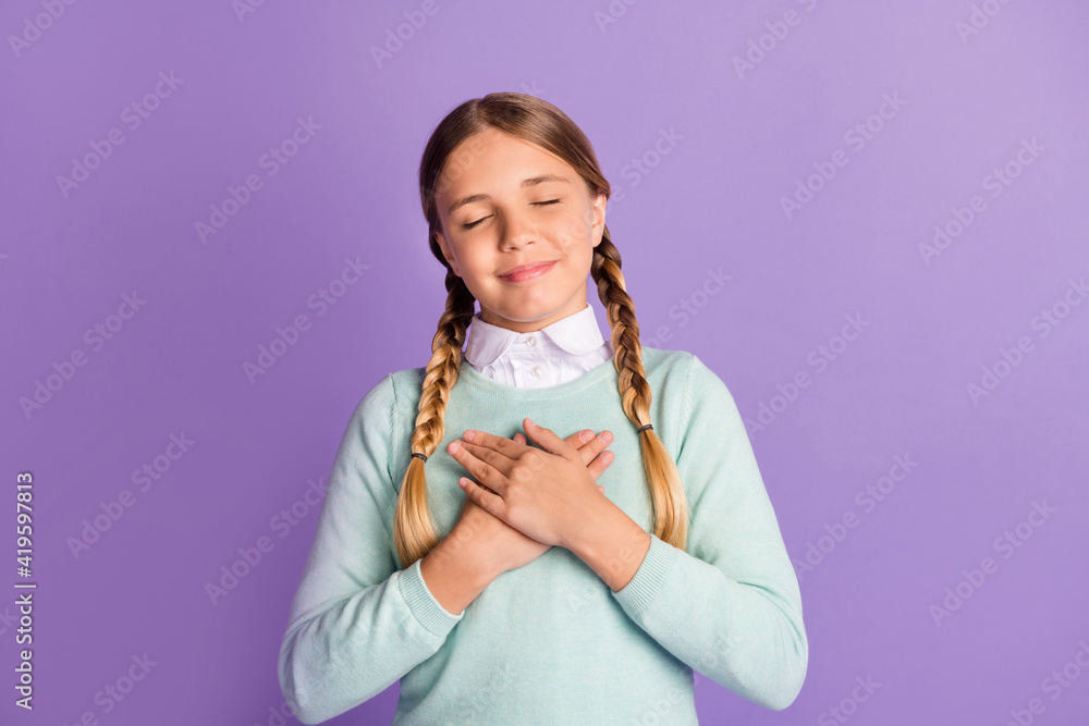 Photo of small grateful girl closed eyes crossed hands chest wear green sweater isolated purple background Photo of small grateful girl closed eyes crossed hands chest wear green sweater isolated purple background