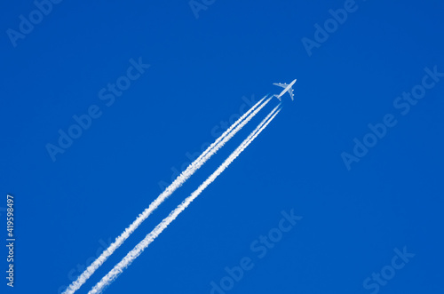 White airplane flies in the blue sky leaving a contrails behind it