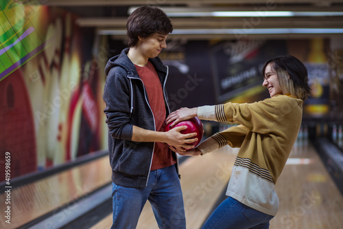 Young couple standing in a bowling alley and fighting for a ball.