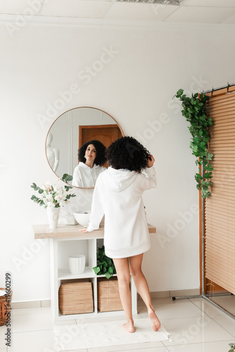 Woman with african curls touching her hair while standing in front of the mirror