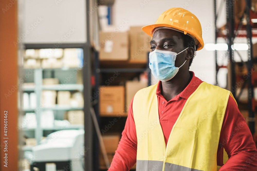 African man working inside warehouse while wearing safety mask during coronavirus outbreak - Focus on face African man working inside warehouse while wearing safety mask during coronavirus outbreak - Focus on face