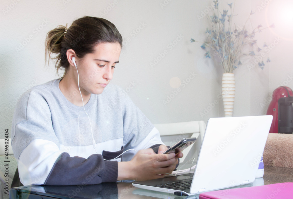 Attractive cheerful young brunette businesswoman sitting at the table with laptop computer indoors, wearing wireless earphones, audio call, waving hand Attractive cheerful young brunette businesswoman sitting at the table with laptop computer indoors, wearing wireless earphones, audio call, waving hand