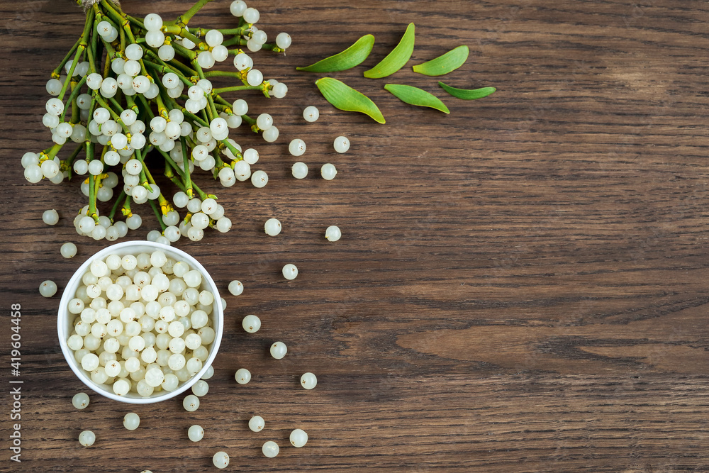 container with mistletoe fruit and branches of evergreen white mistletoe on a wooden surface, top view container with mistletoe fruit and branches of evergreen white mistletoe on a wooden surface, top view
