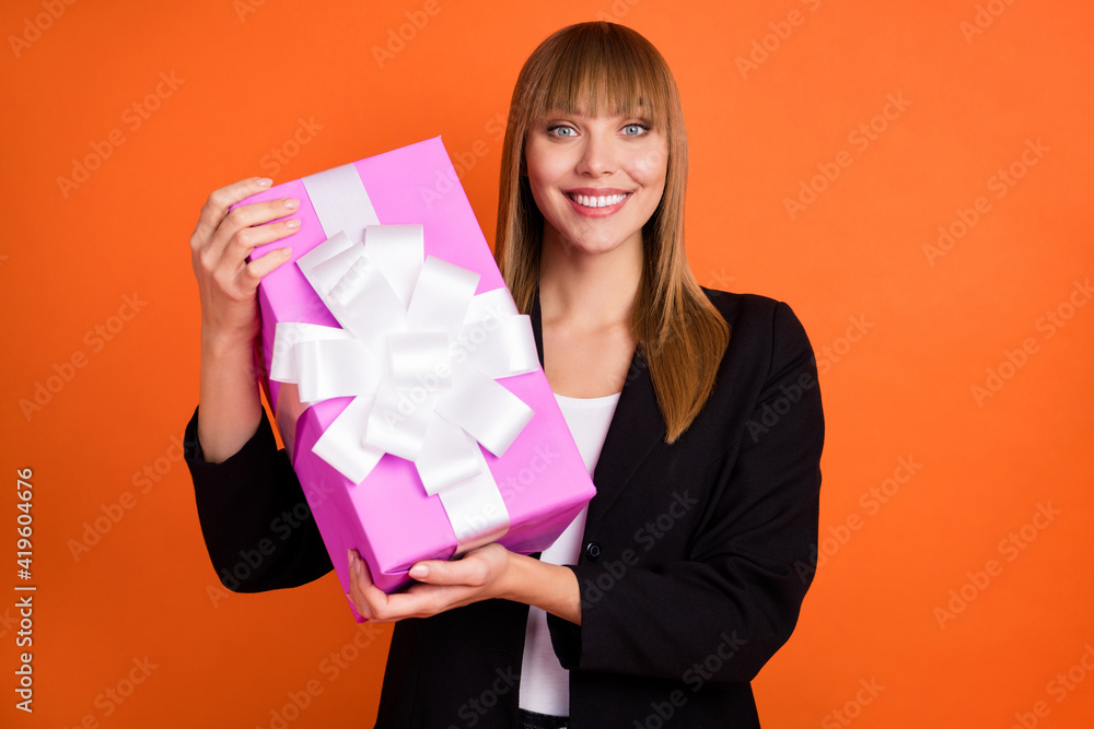 Portrait of charming cheerful girl holding in hands festal giftbox isolated over bright orange color background Portrait of charming cheerful girl holding in hands festal giftbox isolated over bright orange color background