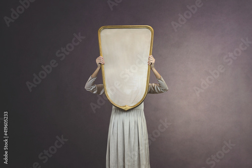 Photography woman hides holding a mirror in front of her face; introspection concept
