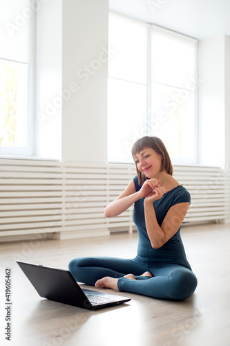 Woman in sportswear sits in front of a laptop and shows her hands a heart