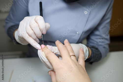 client is undergoing a procedure with a manicure master. Manicurist apply gel polish to nails