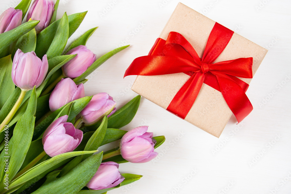 Tulips and gift box on a white background. Festive floral concept with clean text space. Flat lay. View from above. Tulips and gift box on a white background. Festive floral concept with clean text space. Flat lay. View from above.