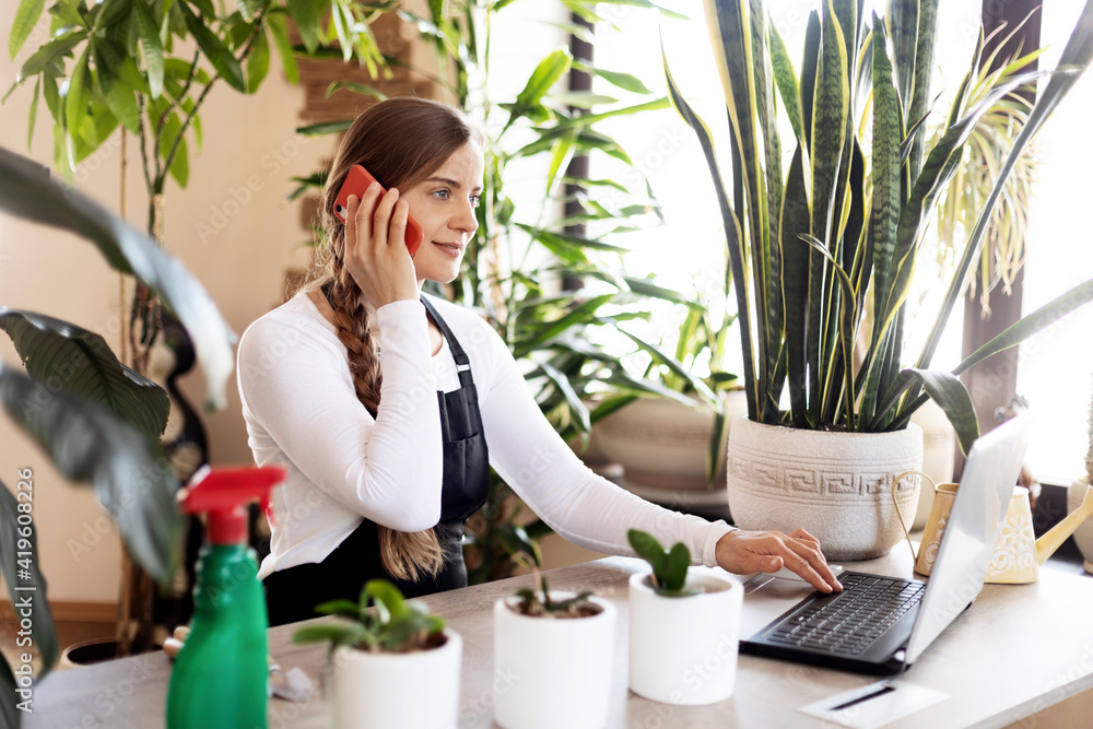 Portrait of young female florist talking on phone and using laptop at flower shop. Portrait of young female florist talking on phone and using laptop at flower shop.
