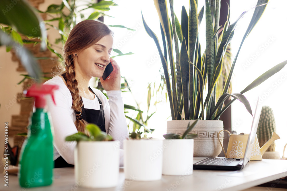 Portrait of a young female florist talking on the phone and using a laptop in a flower shop. Portrait of a young female florist talking on the phone and using a laptop in a flower shop.