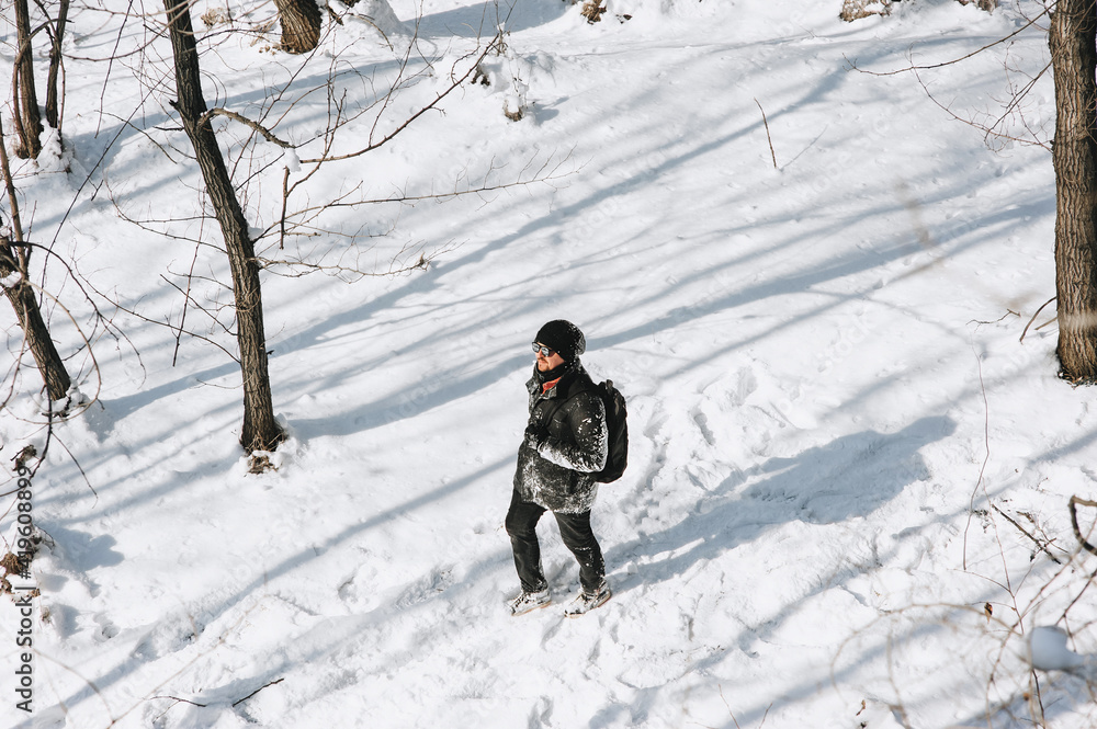 A young man, a wanderer, a tourist in black clothes with a backpack on his back walks through the snowy forest, enjoying the beautiful nature and fresh air. Photography, concept.