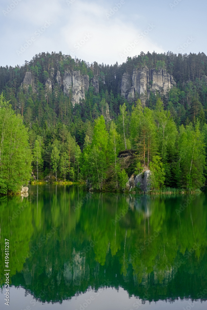 The green forest is reflected in the water. Rock on the lake shore. Summer landscape