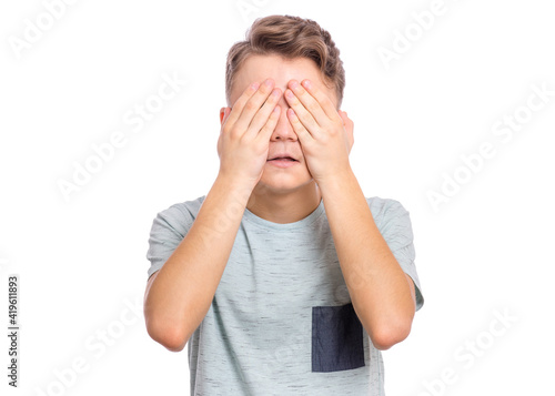 Handsome teen boy with sad expression covering face with hands while crying, isolated on white background