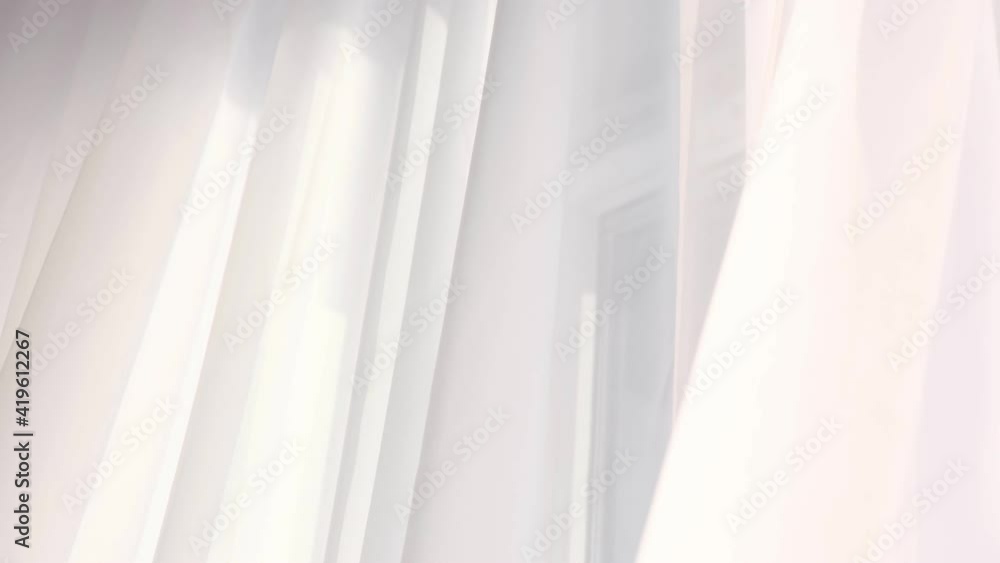Bright morning sun in the open window through the curtains. Abstract white waving curtain in white bedroom apartment. Bright morning sun in the open window through the curtains. Abstract white waving curtain in white bedroom apartment.