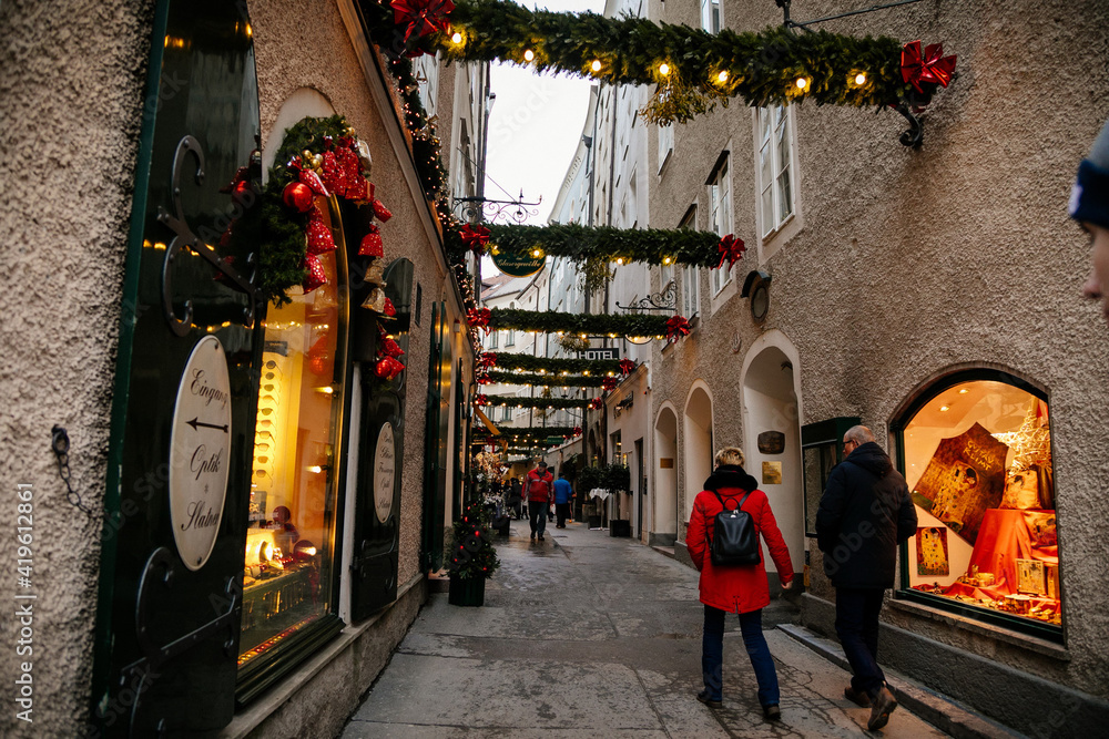 Fototapeta premium Handcrafted colorful holiday decoration at Goldgasse or Golden Street, old town, traditional advent, green Christmas tree branches outdoors in the center of Salzburg, Austria