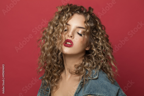 Attractive young woman with curly hair on red background