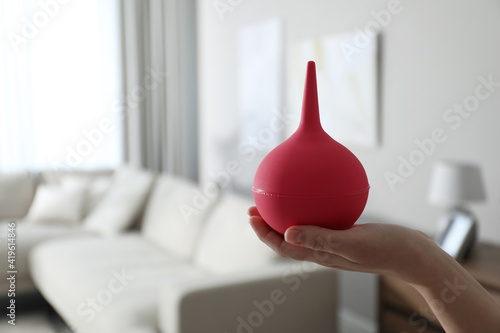 Woman holding pink enema at home, closeup. Space for text photo