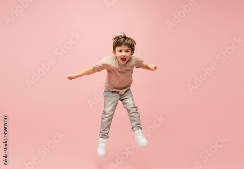 Flying high. Happy, smiley little caucasian boy isolated on pink studio background with copyspace for ad. Looks happy, cheerful. Childhood, education, human emotions, facial expression concept.