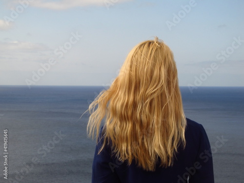 Dziewczyna z blond włosami patrze daleko w horyzont nad morzem