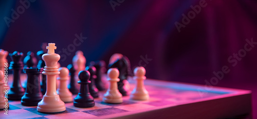 Valokuva Chess pieces on a chessboard on a dark background shot in neon pink-blue colors