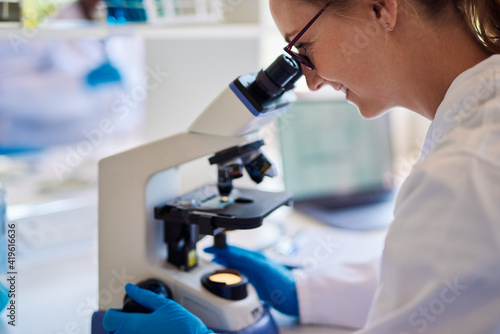 Smiling female lab technician looking at samples under a microscope