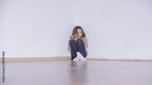 Frightened child sitting in the corner, hugging teddy bear toy, punishment