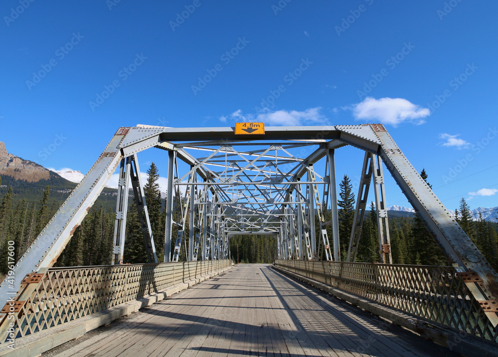Old steel road bridge weather beaten blue grey colour against a deep blue sky. 