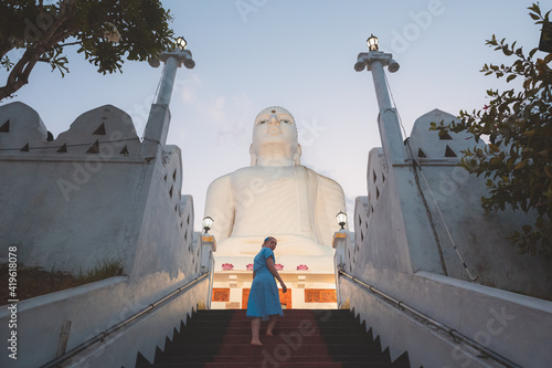 Photography A young female caucasian tourist ascends the steps to the giant white Buddha statue at Sri Maha Bodhi Viharaya, a Buddhist temple at Bahirawakanda in Kandy, Sri Lanka