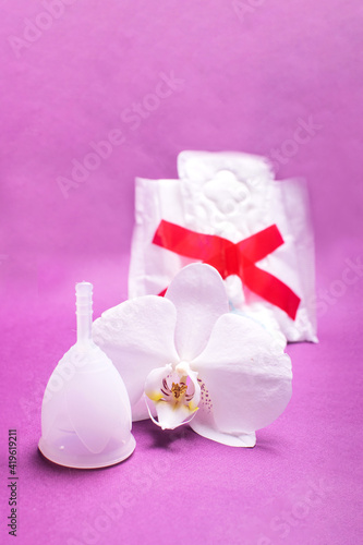 Eco-friendly siliconemenstrual cup with pad and tampon on pink background.