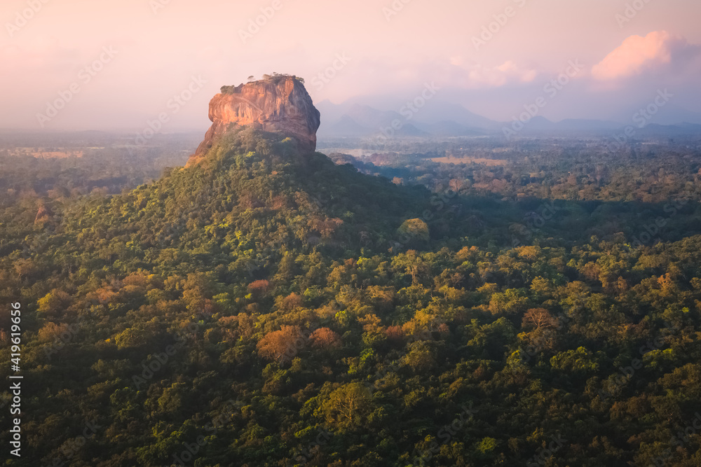 Jungle landscape view of the ancient Sigiriya rock fortress from Pidurangala Hill in Sri Lanka with colourful sunset or sunrise light.