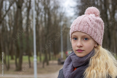 Photo portrait of a girl in a white sweater, the blonde holds the neck of the sweater and looks at the camera. Pretty woman in the park in autumn. Autumn fashion and style.