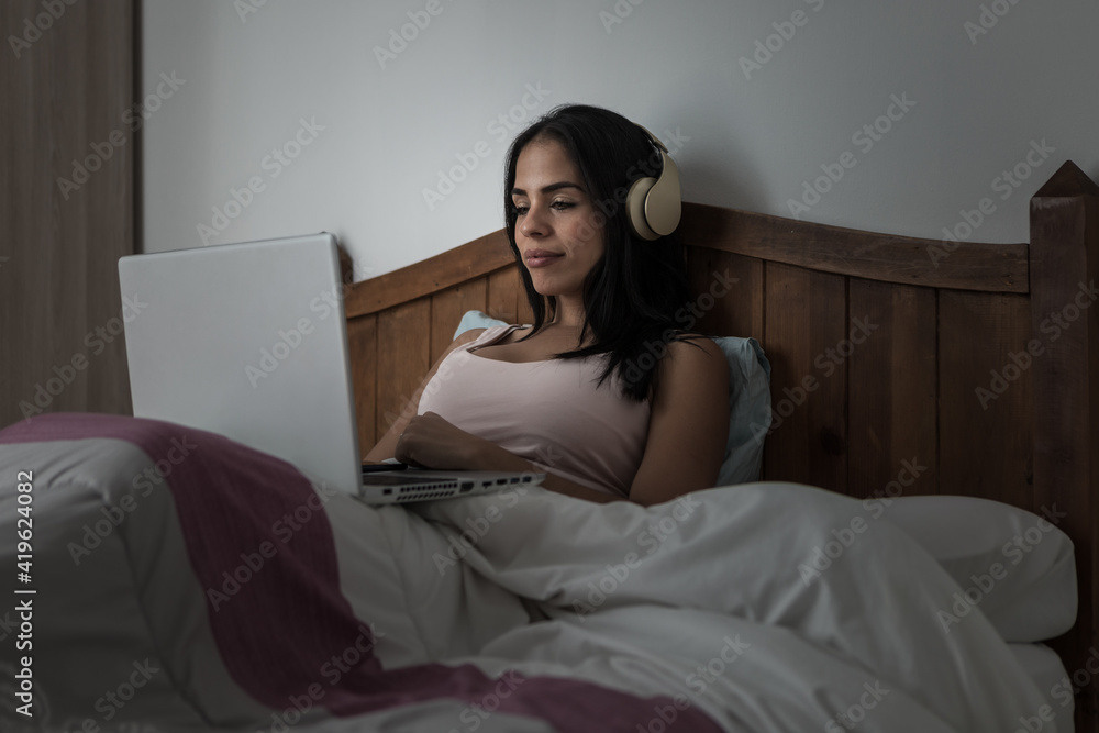 Woman in headphones using laptop in bed Woman in headphones using laptop in bed