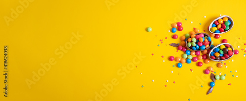 Banner. Chocolate Easter eggs with colored candies on a yellow background.