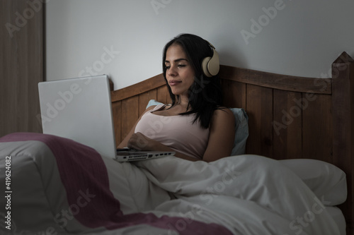 Woman in headphones using laptop in bed